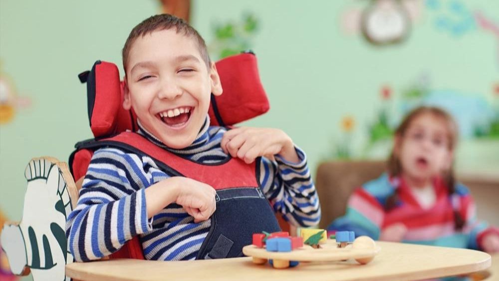 a photo of a young boy with cerebral palsy smiling at a table full of toys