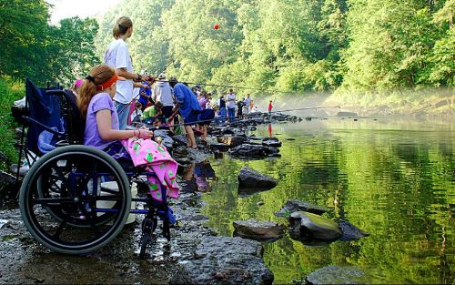 a photo of a group of people fishing in a river, one girl is using a wheelchair