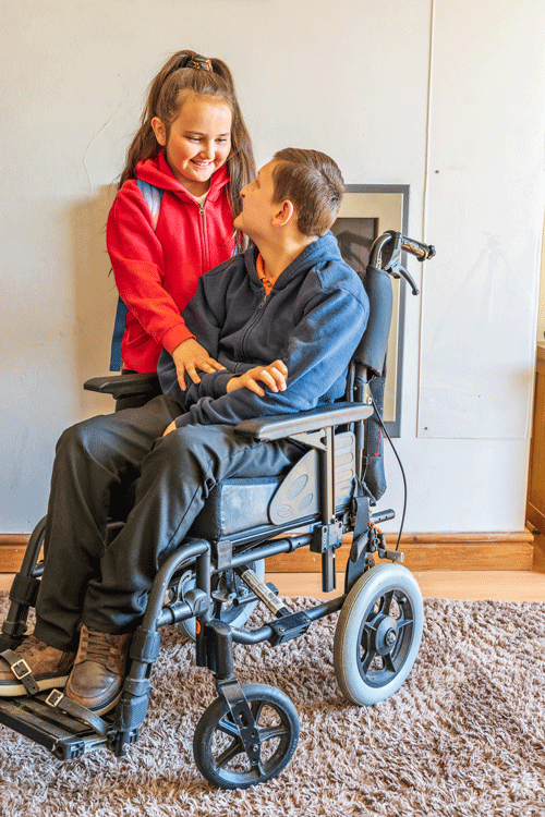 a brother and sister posing beside each other, the brother is sitting in a wheelchair