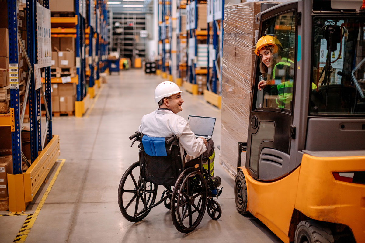 a man in a wheelchair talking to a woman operating a forklift in a warehouse