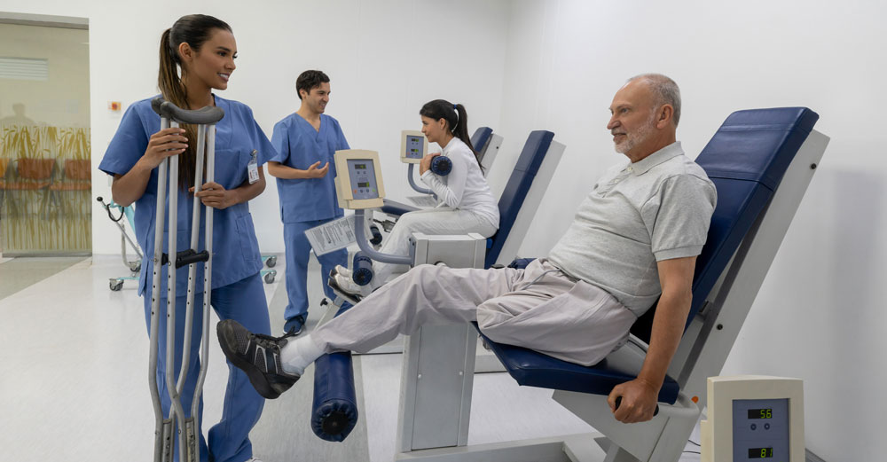 Patient performing leg exercise on rehabilitation machine with healthcare staff nearby