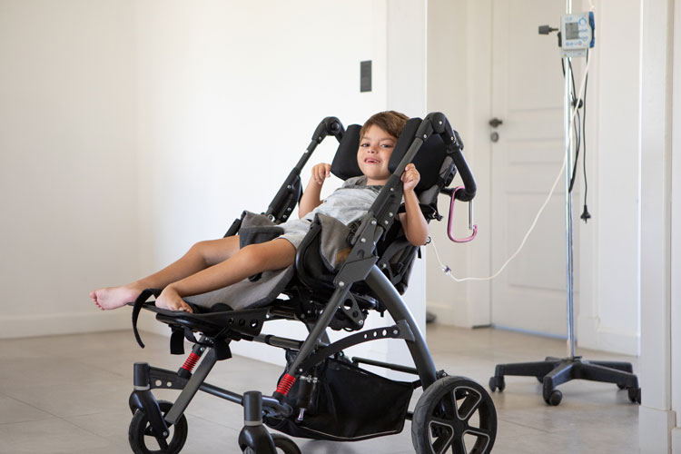 Child seated in an adapted mobility chair in a home or clinical setting with medical equipment nearby